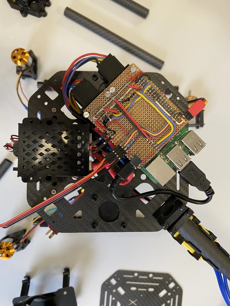 Electronics detail — custom PCB mounted directly on top of the Raspberry Pi, connected via GPIO. Pixhawk 4 Mini autopilot visible in its 3D-printed mount on the left. ESC signal wiring and motor cables routed across the bottom plate.